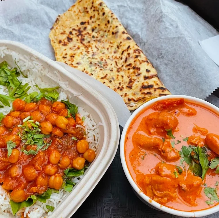Chana masala over rice with a paratha and a bowl of butter chicken