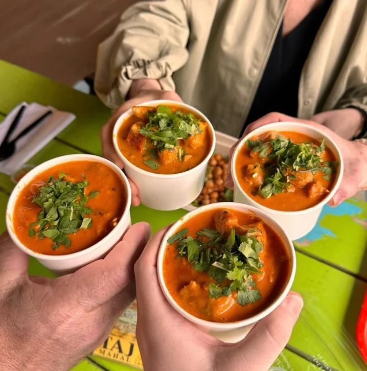 Four hands raising bowls of curry over a green patio table